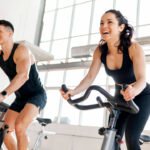 athletic couple of cyclists train on static bicycle simulator, man trainer and fitness woman go in for sports together